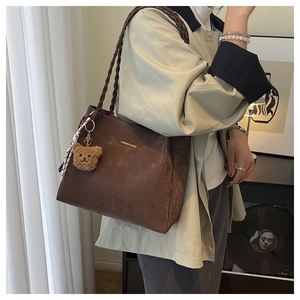 Detail of dark brown tote bag featuring woven handles and stylish bear charm with silk scarf