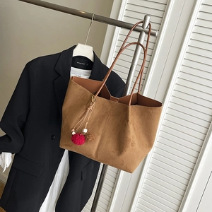 Borsa tote marrone opaca con spalline e ciondolo appesa a una gruccia minimalista