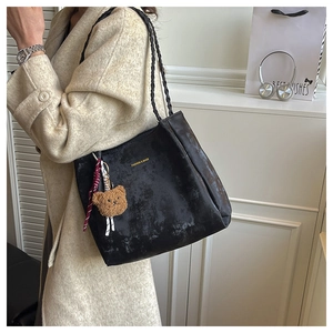 Detail of black matte leather tote bag with braided strap and plush bear pendant