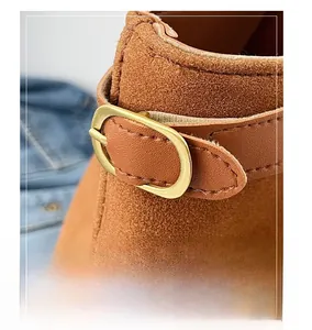 Detail of brown suede leather boots featuring an oval gold metal buckle and stitching