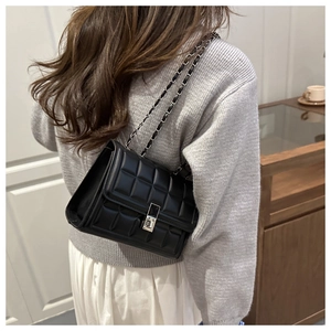 Detail of classic black quilted shoulder bag with silver chain strap and metal turn-lock