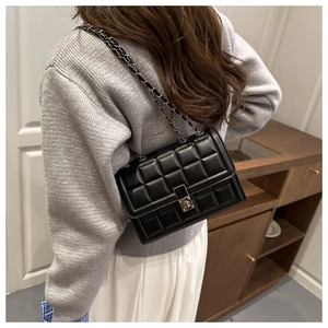 Detail of black quilted leather shoulder bag with silver chain strap and metal turn-lock