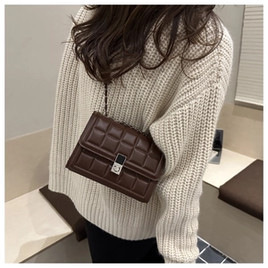 Detail of coffee brown quilted crossbody bag with metal lock and chain strap