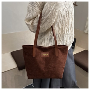 Detailed close-up of dark brown suede tote bag featuring a gold fashion embossed patch