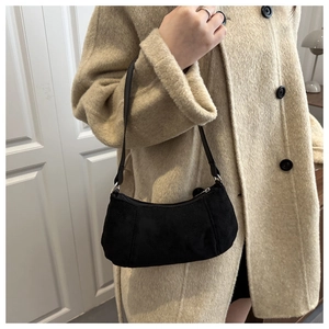 Détail du sac croissant en daim noir minimaliste porté sur un manteau en laine beige chic