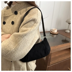 Détail d'un sac hobo noir mat avec fermeture éclair argentée porté avec un manteau beige