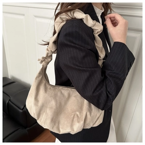 Close-up of beige corduroy dumpling bag with ruched strap on a model wearing a blazer