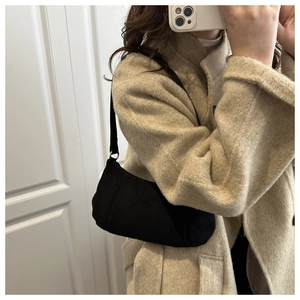 Détail d'un sac à bandoulière minimaliste en daim noir porté avec un manteau beige
