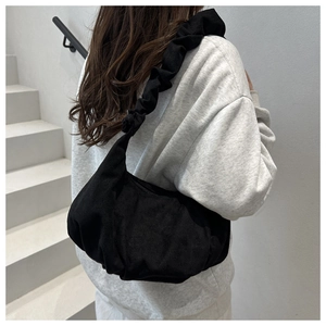 Detail of a black scrunchie-style shoulder bag with elegant pleated textures and soft suede fabric