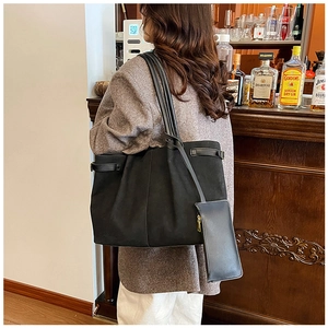 Detail of matte black tote bag with long straps and mini pouch worn in warm bar setting