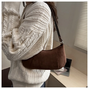Gros plan d'un sac baguette en cuir dépoli marron foncé porté avec un pull en maille blanc