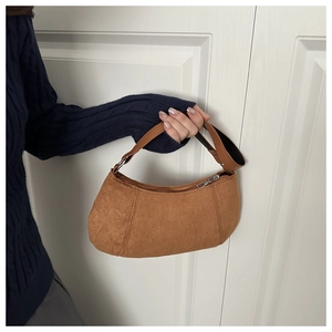 Détails du matériau en daim marron et de la fermeture éclair argentée de ce sac demi-lune