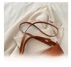 Detail of brown suede shoulder bag with dual leather straps and metallic buckles
