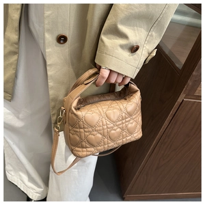 Brown heart-quilted leather tote bag worn by a model in a beige trench coat