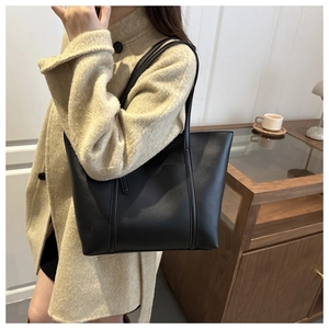 Detail of minimalist black tote bag on model showing large capacity and soft PU leather texture