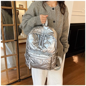 Detail of silver metallic puffer backpack featuring woven zipper pulls and stitched pockets
