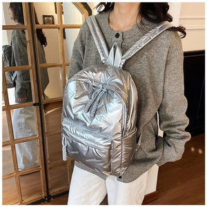 Silver metallic padded backpack shown on a model in a cozy indoor minimalist setting