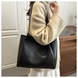 Close-up of a minimalist black tote bag with slender straps worn by a model in a room