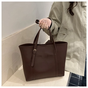 Détail d'un sac cabas en cuir marron foncé montrant la poche avant et le fermoir doré