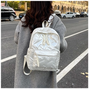 Detail of white quilted down backpack featuring woven rope zippers and puffer texture