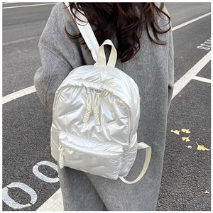 Outdoor view of a white quilted puffer backpack with V-shaped stitching on a grey coat