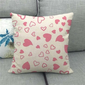 Detalle de funda de cojín de lino con corazones rosas sobre un sofá de tela gris