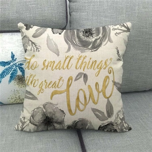 Leinen Kissenbezug mit grauen Blumenmustern und goldener Aufschrift auf einem grauen Sofa