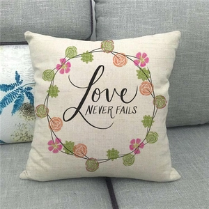 Detail eines Leinenkissenbezugs mit Love Never Fails Text und Kranz auf Sofa