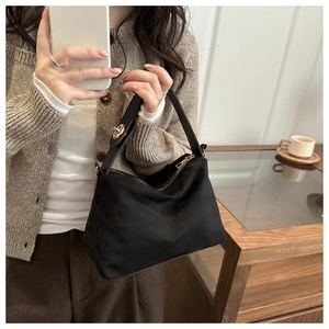 Detailed shot of black suede handbag with gold circular metal buckle and zipper closure