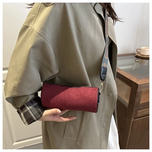 Close-up of burgundy cylindrical crossbody bag with ethnic patterned wide strap and matte finish