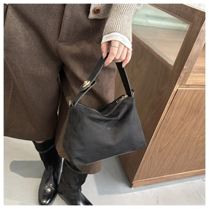 Detail of black faux suede shoulder bag with gold zipper held by a model in casual wear