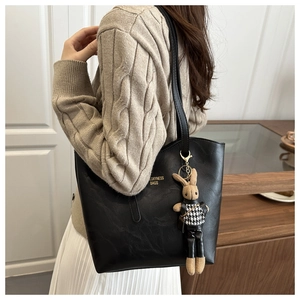 Close-up of black leather tote bag with gold logo and plush rabbit charm detail