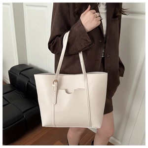 Detail of a creamy white leather tote bag with a front pocket and gold hardware straps