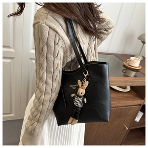 Detail of black tote bag with gold logo and cute bunny pendant on model shoulder