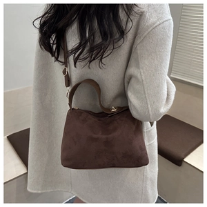 Deep brown suede shoulder bag worn with cream coat, showing texture and golden hardware