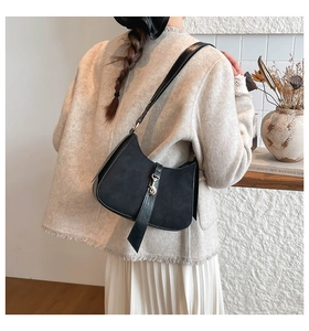 Detail of black suede and smooth leather crescent bag with gold buckle on shoulder