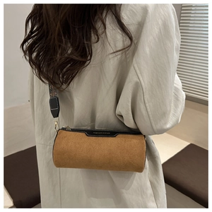 Detail of a brown suede cylinder bag featuring a wide jacquard strap and gold zipper