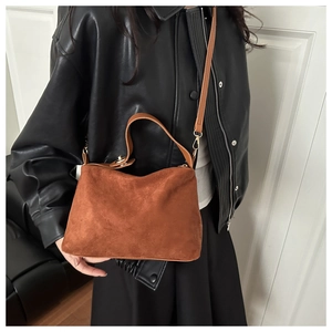Detail of brown suede tote bag featuring smooth leather handles and gold metal hardware