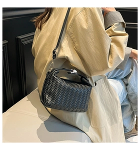 Close-up of black woven shoulder bag featuring textured V-pattern and gold hardware details