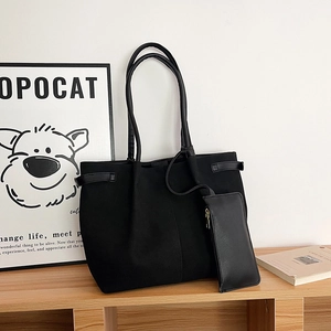 Minimalist black tote bag with matching pouch on a wooden shelf in a cozy room