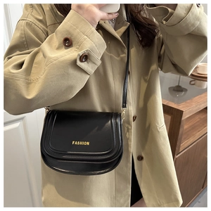 Detail of a black leather saddle bag with gold FASHION lettering on a khaki coat