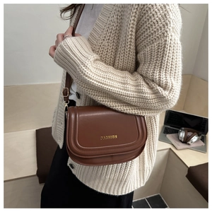 Close-up of a brown saddle crossbody bag with gold Fashion text on adjustable leather strap