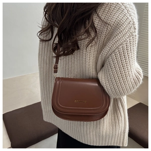 Detail of dark brown saddle bag with golden FASHION metal lettering on leather flap