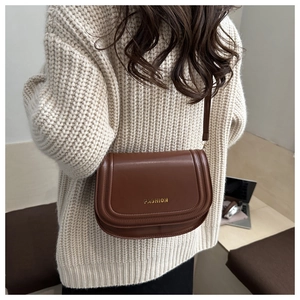 Detailed view of a brown faux leather crossbody bag with a golden fashion logo detail