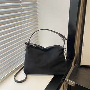 Minimalist black faux suede shoulder bag with gold hardware on a clean white windowsill