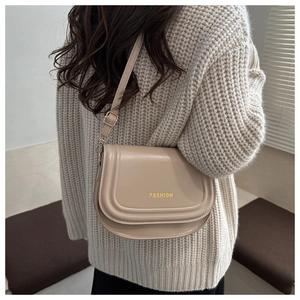 Detail shot of a beige faux leather saddle bag with gold logo on knit sweater background