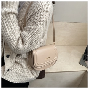 Detail of a beige PU leather crossbody saddle bag featuring gold FASHION letter branding