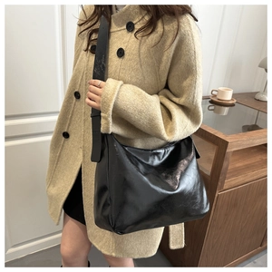 Détail d'un sac à bandoulière en cuir noir brillant montrant la texture sur un modèle