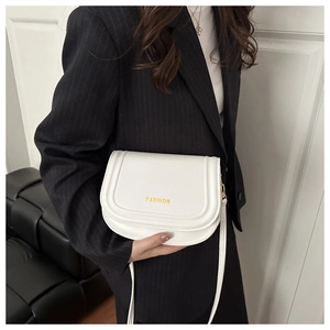Detailed close-up of a white leather saddle bag featuring gold FASHION lettering