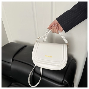 Detailed shot of a white saddle bag featuring a gold FASHION logo on a black sofa
